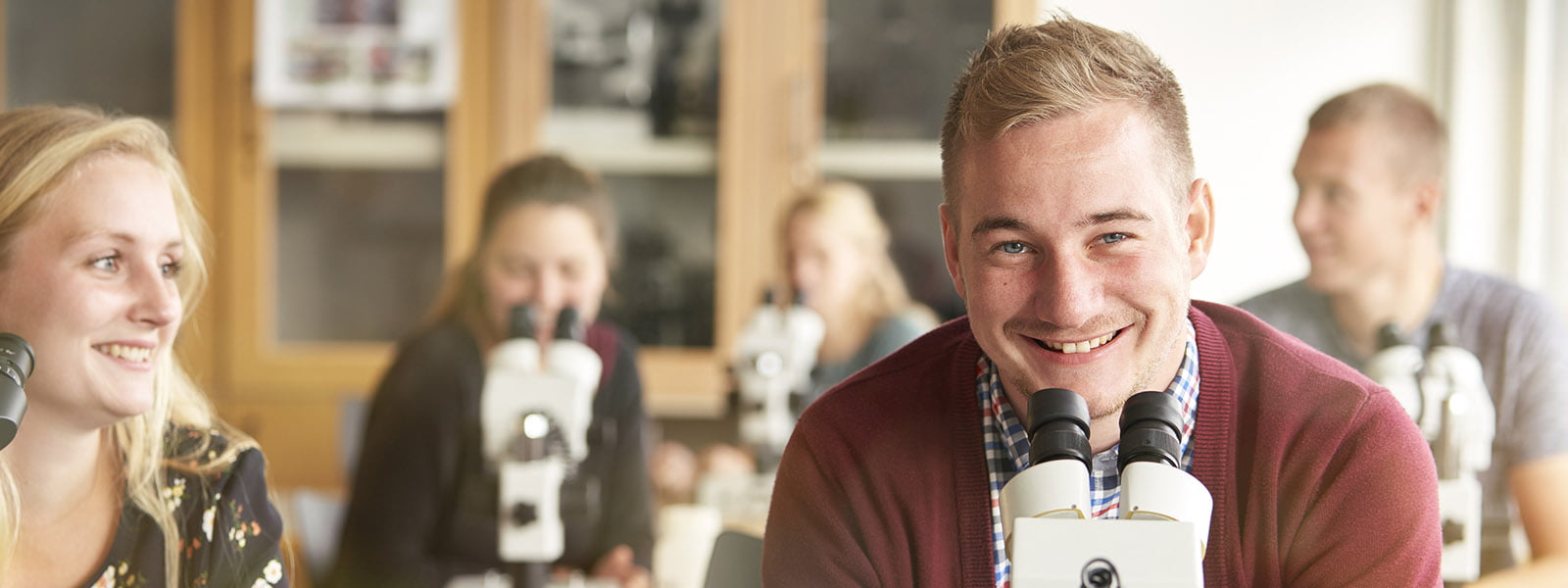 klasseværelse med smilende studerende foran mikroskoper