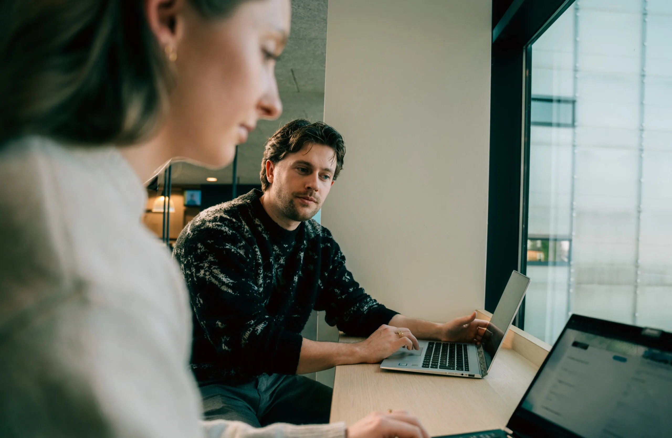 To studerende sidder ved et bord og arbejder ved deres computere.